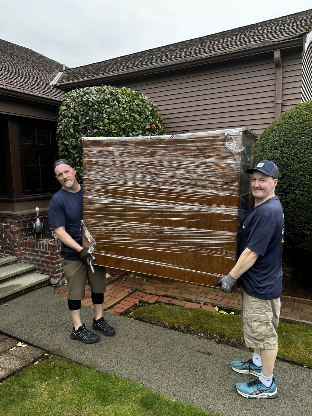 Lake Union Movers crew carrying a shrink-wrapped cabinet from a home
